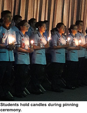 Students hold candles during pinning ceremony.