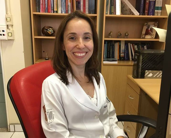 Fernanda Fernanda Raphael Escobar Gimenes de Sousa, PhD, MSN, BSN, sits in her office wearing her lab coat.