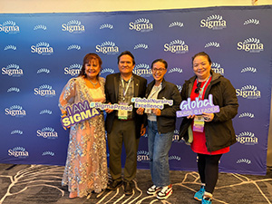 Four members, three women and one man, hold Sigma props for a photo op.